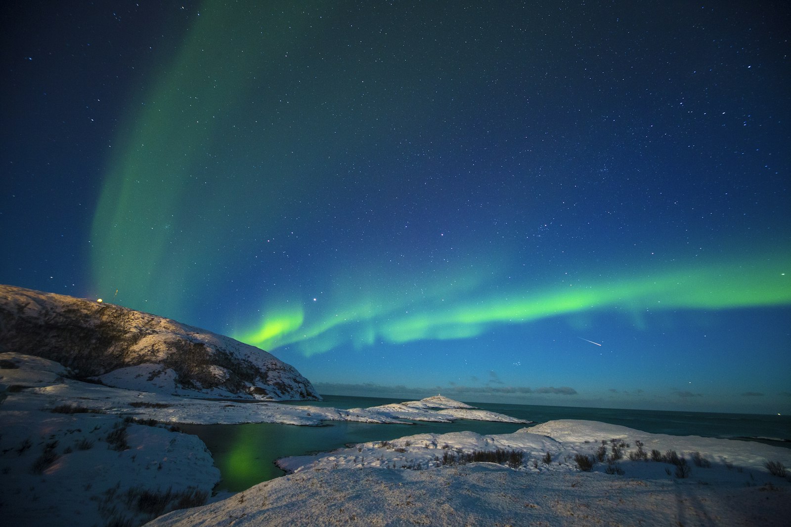 Green aurora borealis over a snowy coastline and sea near Tromsø, Norway